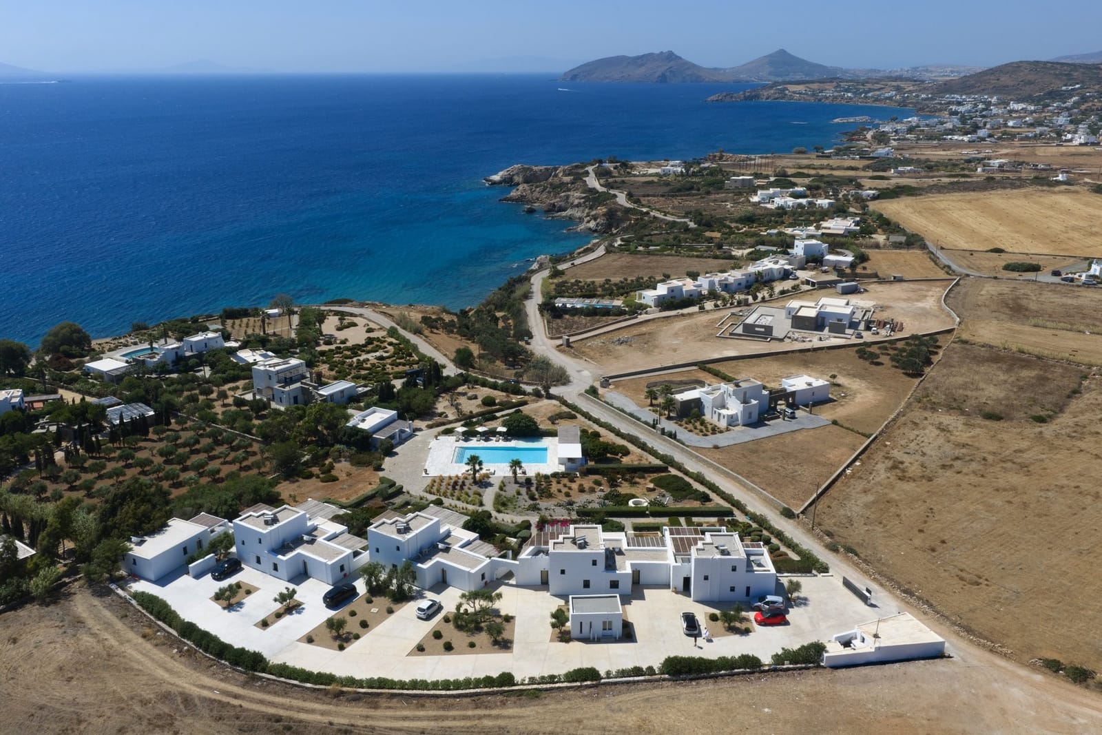 Aerial view of the Stagones estate on the Ampelas shoreline, white residences around a long pool with Naxos on the horizon