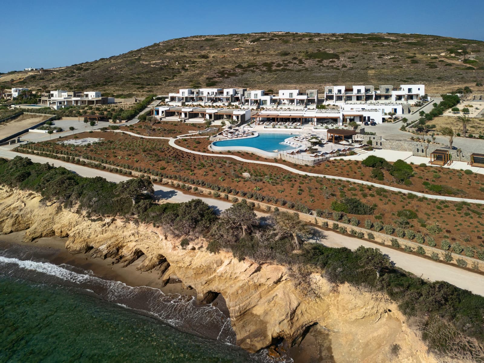 Aerial view of Hotel Vione Paros at Ampelas, white terraced buildings above the pool and the rocky shoreline
